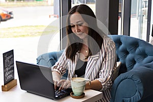 Gorgeous young business woman working remotely while sitting in front of an open laptop computer in the interior of a modern cafe