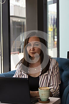 Gorgeous young business woman working remotely while sitting in front of an open laptop computer in the interior of a modern cafe