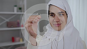 Gorgeous young Middle Eastern woman with hazel eyes in white hijab admiring engagement ring in hand. Portrait of happy