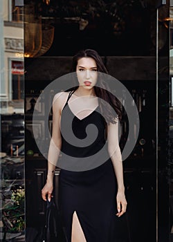 Gorgeous young model woman with perfect dark hair looking at camera posing in the city wearing black evening dress
