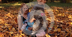 Gorgeous young mother with two kids enjoying sunny autumn day on the foliage.