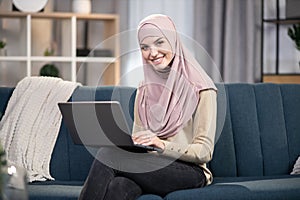 Gorgeous young Muslim woman wearing hijab, using laptop at home, shopping online, working or studying. Muslim woman