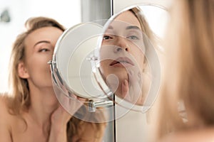 Gorgeous young naked woman looking at mirror.