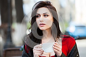 Gorgeous young woman with cup of coffee in city street. Coffee break. Stylish hipster girl drinking coffee in street.