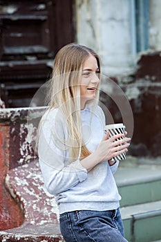 Gorgeous young woman with cup of coffee in city street. Coffee break. Coffee to go. Stylish hipster girl drinking coffee in street