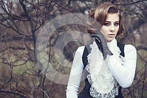 Gorgeous young woman with elegant Victorian hairstyle holding her hand in leather glove at her cheek