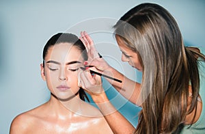 Gorgeous young woman face portrait. Makeup artist applies eye shadow. Hand of visagiste, painting cosmetics of young