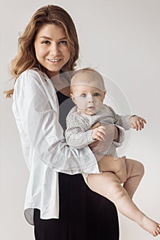 Gorgeous young woman is holding an adorable toddler in arms, smiling, posing. Beautiful mother and cute little daughter