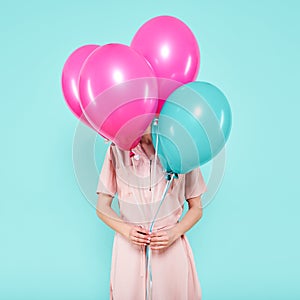 Gorgeous young woman in party outfit holding bunch of colourful balloons, isolated over pastel blue colored background. Birthday.