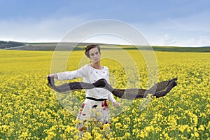 Gorgeous young woman playing with scarf in a canola field