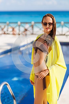 Gorgeous young woman posing in bikini with yellow pareo near swimming pool