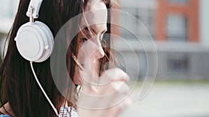 Gorgeous young woman in a trendy look, uses her phone, turns on the music, listens to the music with white headphones