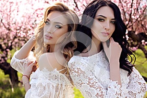 gorgeous young women in elegant dress posing in garden with blossom peach trees