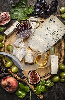 Gorgonzola and Camembert cheese with Knife for cheese white and dark grapes, honey and jam on wooden cutting board on a dark ru