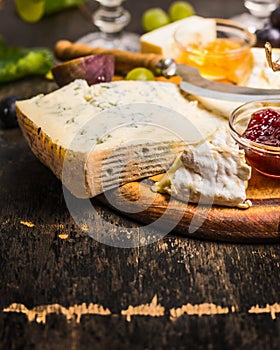 Gorgonzola Camembert on a wooden cutting board with a knife for cheese with honey and jam light grape on dark wooden background cl