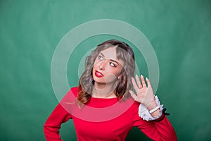 Gossip concept. Colorful studio portrait of pretty young woman with palm near her ear. pretty woman in red dress holds