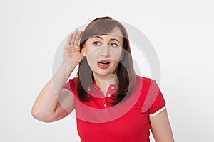 Gossip concept. Portrait of pretty middle aged woman with palm near her ear. Red blank shirt. Copy space and mock up