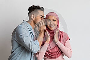 Gossips Concept. Cheerful arab guy whispering something into his muslim girlfriend's ear