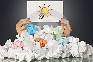 Got an idea with light bulb in womanâ€™s hand, behind a pile of crumpled paper