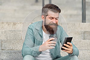 Got SMS online. Happy man read SMS drinking coffee outdoors. Sending and receiving SMS via smartphone. Mobile