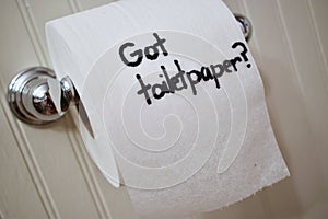 `Got Toilet Paper`, written in sharpie on cardboard toilet paper roll that is left hanging on the spool, on the wall