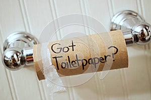 `Got Toilet Paper`, written in sharpie on cardboard toilet paper roll that is left hanging on the spool, on the wall photo
