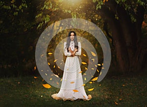 Gothic art photography fantasy woman creates magic. Bright divine light, autumn yellow leaves soar rotate fly in wind