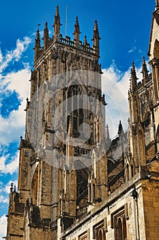 Gothic cathedral tower against a blue sky with clouds, showcasing intricate architectural details and flying buttresses in York,