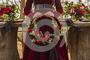 Gothic girl bride wearing a red brocade dress holds a wreath of