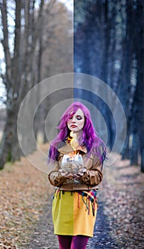 Gothic Girl with purple hair is standing with a burning glass in her hands in the alley in the autumn forest. Concept editing, pho