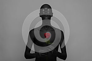 Gothic and Halloween theme: a man with black skin holding a red rose, black death isolated on a gray background in studio