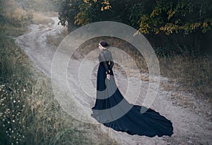 Gothic lady from old horror movie. Walks along the road in the autumn forest.