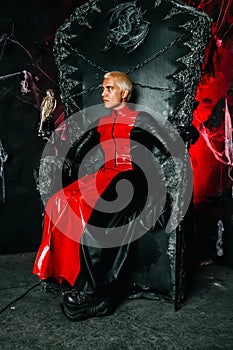 Gothic man with scary bloody makeup and bird of prey on huge scary throne ready for Halloween party