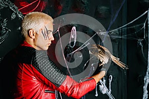 Gothic man with scary bloody makeup and bird of prey on huge scary throne ready for Halloween party