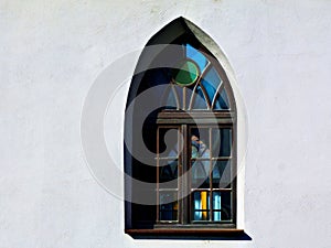 Gothic shape church window with pointy arch and colorful glass in white stucco wall