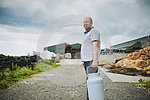 Gotta get this to where it needs to go. Cropped portrait of a male farmer carrying a milk can on his dairy farm.