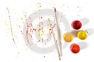 Gouache jars and paint brushes on a white background with colorful spray in top view