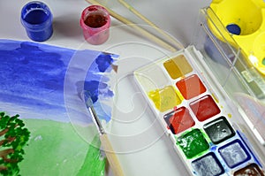 gouache paint brushes and children's drawings. photo child paints a brush with watercolor honey paints. children's art