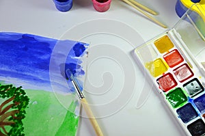 gouache paint brushes and children's drawings. photo child paints a brush with watercolor honey paints. children's art