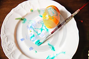 A gouache-painted yellow Easter egg on a white plate with a tassel