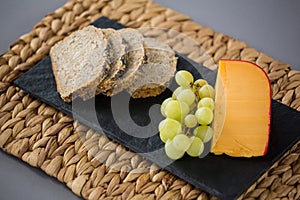 Gouda cheese, bread slices and grapes on slate plate