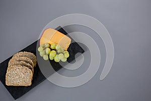 Gouda cheese, grapes and brown bread slices on slate plate