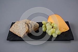 Gouda cheese, grapes and brown bread slices on slate plate