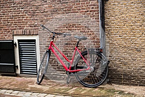 Gouda, South Holland/The Netherlands - February 15 2020: black and bright red bike locked to a drain pipe in front of a brick wall