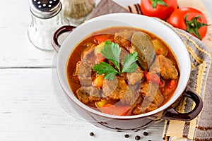 Goulash in ceramic bowl on white wooden background. Traditional hungarian soup.