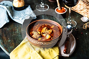 Goulash or stew in copper pan with spoon on rustic kitchen table. Eintopf, chili con carne. Traditional hungarian dish. Homemade