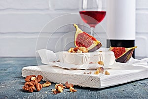 Gourmet appetizer of white brie cheese or camembert with fresh figs, nuts and red wine on wooden cutting board