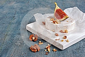 Gourmet appetizer of white brie cheese or camembert with fresh figs and nuts on wooden cutting board