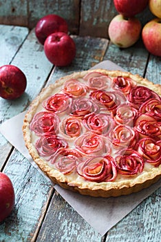 Gourmet apple pie. Open pie with red apple roses and cream filling served with organic apples on shabby blue wooden table