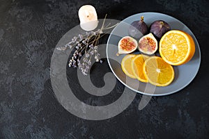 Gourmet dish with exotic fruits, orange and figs on a gray plate on a black background
